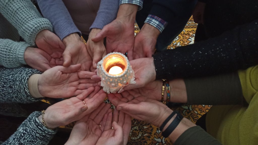 Na zdjęciu widać dłonie uczestników trzymające wspólnie lampion z zapaloną świeczka